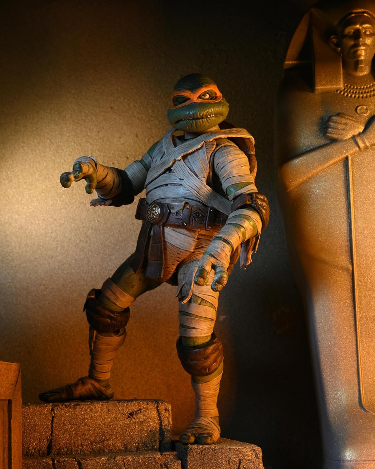 : A dynamic action pose of the NECA Michelangelo as The Mummy figure, demonstrating its range of articulation and weathered paint application.