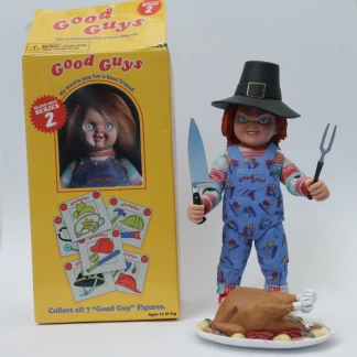 The Thanksgiving Chucky action figure wearing a pilgrim hat and holding carving tools, standing next to a turkey platter and an opened yellow Good Guy box.
